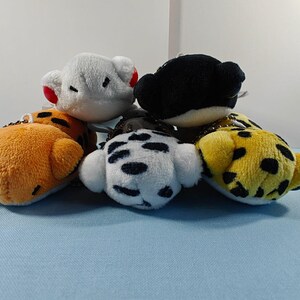 May include: A collection of small, plush animal head keychains. The keychains include a white bear with red ears, an orange tiger, a black bear, a white dalmatian, and a yellow leopard with black spots.