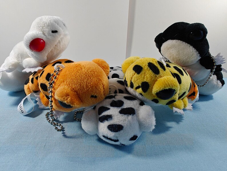 May include: A collection of plush animal keychains in various designs. Includes a white bird with a red beak, orange and yellow spotted animals, a black and white frog, and a dalmatian dog. Each keychain has a silver chain.