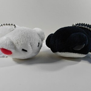 May include: Two plush whale-shaped keychains. One is white with a red mouth and black eyes, the other is black with white accents. Both have silver chain attachments.