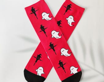 May include: A pair of red socks with a black heel and toe. The socks are patterned with white ghosts and black witch figures. The socks are crossed over each other.