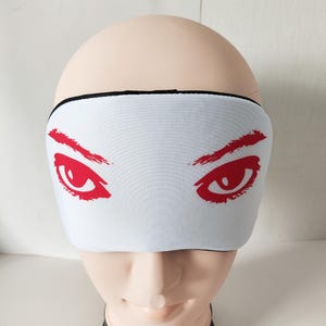 May include: White sleep mask with a black elastic band. The mask has a red print of two eyes with eyebrows.