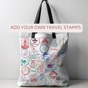 May include: White tote bag with black handles featuring colorful travel stamp designs. The stamps include locations like London, Jamaica, and Arizona, with the text "ADD YOUR OWN TRAVEL STAMPS" across the top. A stylish and practical accessory for travel enthusiasts.