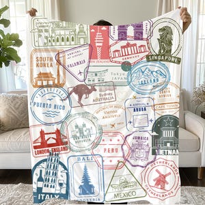 May include: A colorful throw blanket featuring a pattern of vintage passport stamps from around the world. The stamps are arranged in a random pattern and include destinations such as South Korea, Colombia, New Zealand, Germany, Tokyo, Japan, Singapore, Iceland, Australia, Aruba, Cape Town, Jamaica, London, England, Peru, Bali, Italy, Indonesia, Mexico, and Vietnam. The blanket is 60 inches by 80 inches.