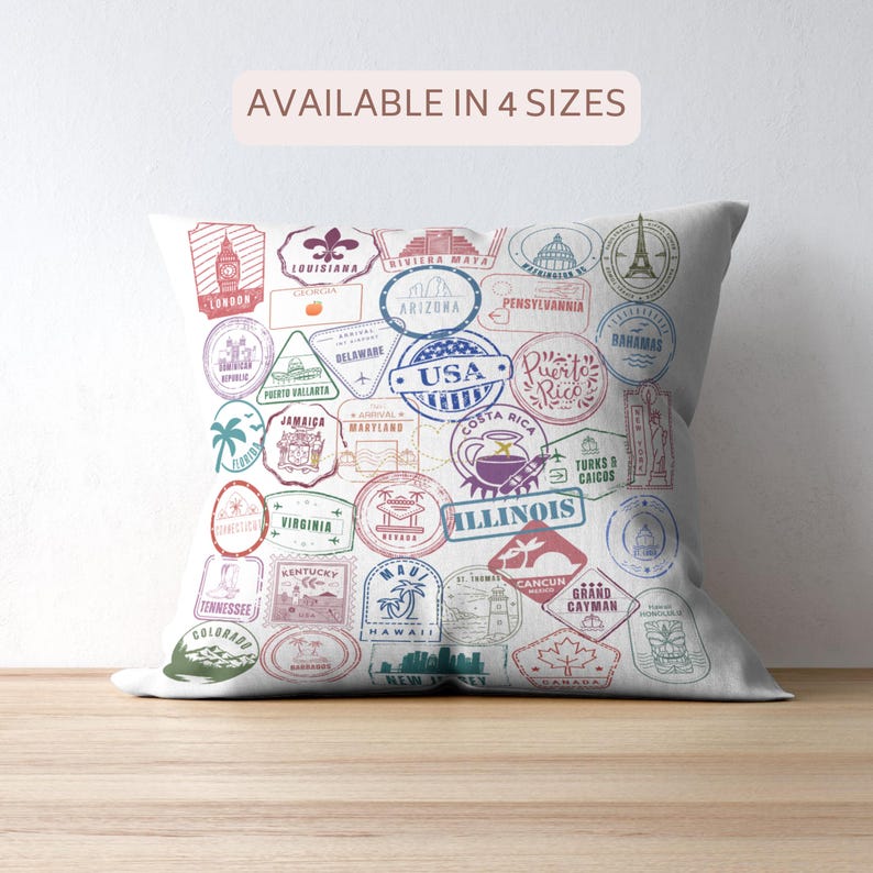May include: A white decorative pillow featuring colorful travel-themed stamps from various locations, including London, Paris, and the USA. The pillow has the text "AVAILABLE IN 4 SIZES" at the top.