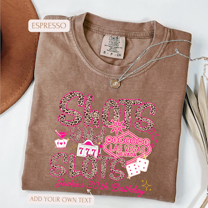 May include: A brown t-shirt with a pink and black leopard print design that says "Shots and Slots" with a Las Vegas welcome sign and dice. The text "Jack's 30th Birthday" is at the bottom of the shirt.