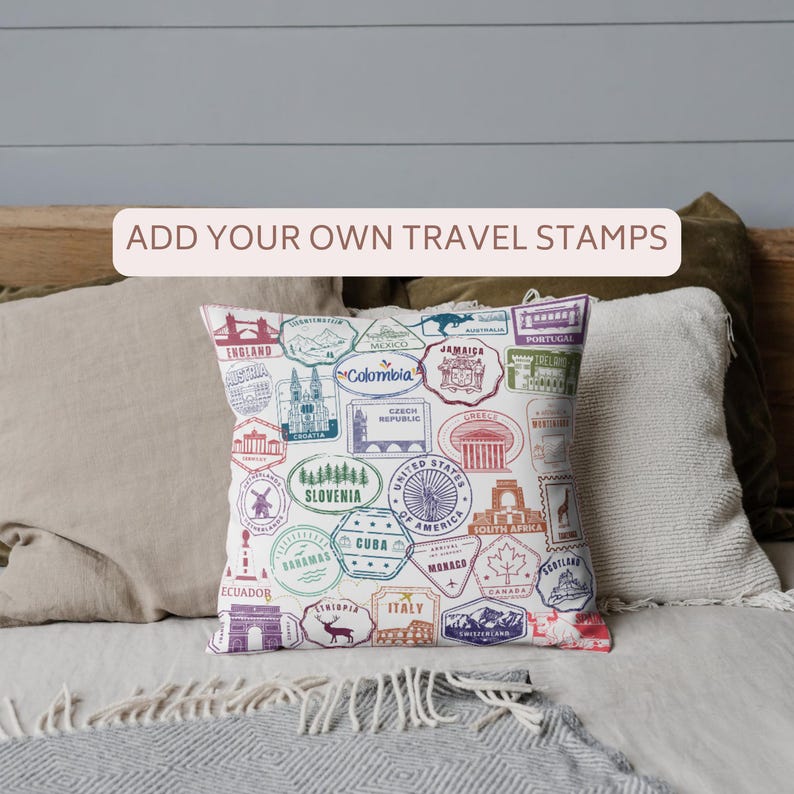 May include: A white square pillow with colorful travel stamp designs from various countries. The pillow features stamps from England, Mexico, Colombia, and more. Text on the pillow reads "ADD YOUR OWN TRAVEL STAMPS".