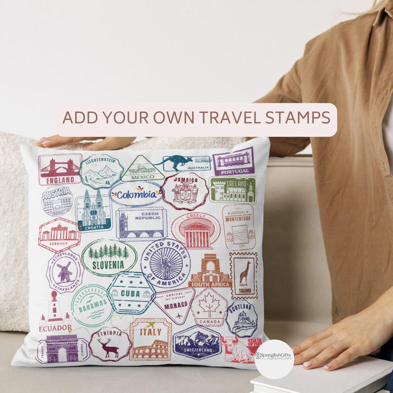 May include: White square pillow with colorful travel stamp designs from various countries. The pillow features stamps from England, Austria, Mexico, Jamaica, Portugal, and more. Text on the pillow reads "ADD YOUR OWN TRAVEL STAMPS."