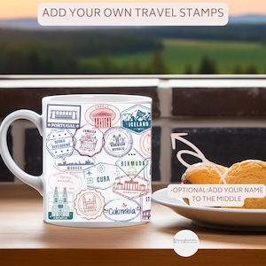 May include: White ceramic mug featuring travel stamps from various countries, including Portugal, Greece, and Iceland. The mug has the text "ADD YOUR OWN TRAVEL STAMPS" and "-OPTIONAL: ADD YOUR NAME TO THE MIDDLE".