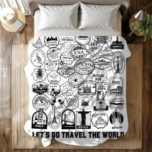May include: White travel-themed blanket featuring black and white illustrations of landmarks and stamps from around the world. Includes text that reads "LET'S GO TRAVEL THE WORLD". The blanket is on a bed with white pillows.