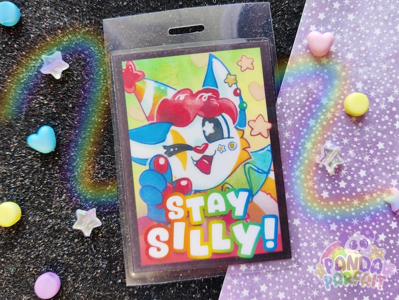 K&ouml;nnte beinhalten: Ein farbenfroher Comic-Charakter mit einer Partym&uuml;tze und einer Clownsnase. Der Charakter h&auml;lt ein Schild mit der Aufschrift "Stay Silly!" Der Hintergrund ist ein gelber und gr&uuml;ner Aquarell-Wasch.
