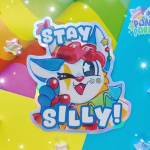 May include: A colorful sticker featuring a cartoon character with a rainbow-colored mane and a red nose. The character is wearing a clown hat and has a happy expression. The sticker says "Stay Silly!" and has a holographic finish.