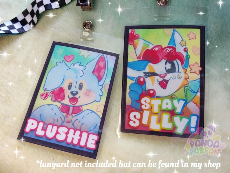 K&ouml;nnte beinhalten: Zwei farbige Cartoon-Charakter-Badgehalter mit schwarzen R&auml;ndern. Der erste Badgehalter zeigt einen blauen und wei&szlig;en Cartoon-Charakter mit rosa Akzenten und dem Text "PLUSHIE". Der zweite Badgehalter zeigt einen roten, wei&szlig;en und gelben Cartoon-Charakter mit dem Text "STAY SILLY!"