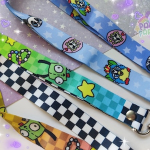 May include: Five colorful lanyards with different cartoon characters and patterns. The lanyards are made of fabric and have a black and white checkered pattern, a green and yellow pattern with a cartoon robot, a blue and green pattern with a cartoon robot, a blue and white pattern with a cartoon character, and a blue and white pattern with a cartoon panda.