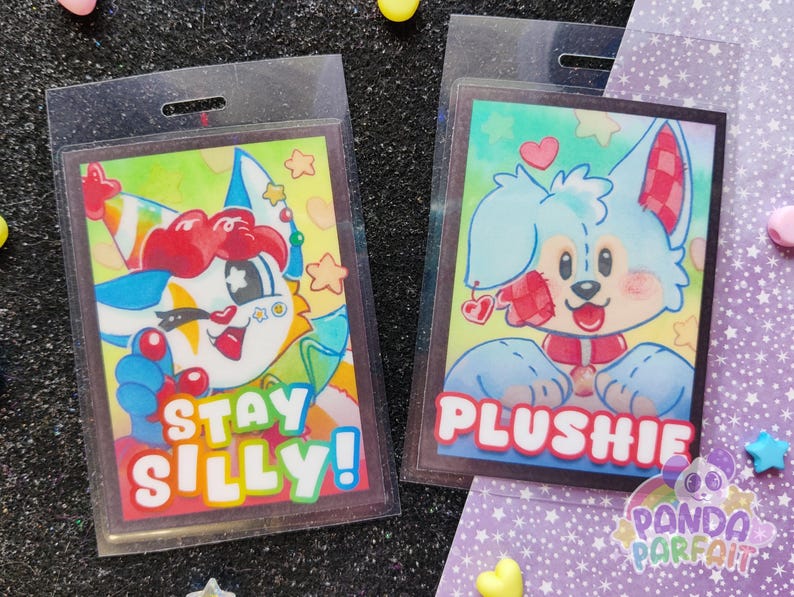 K&ouml;nnte beinhalten: Zwei bunte Badge-Halter mit Cartoon-Charakteren auf wei&szlig;em Hintergrund. Der linke Badge-Halter zeigt einen Cartoon-Charakter mit einem rot-wei&szlig;-blauen Hut und dem Text "Stay Silly!" Der rechte Badge-Halter zeigt einen blauen Cartoon-Charakter mit einer rot-wei&szlig; karierten Schleife und dem Text "Plushie".