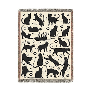 May include: Cream-colored throw blanket with a repeating pattern of black cat silhouettes, paw prints, and fish bones. The blanket has a fringed edge and is suitable for a bed or sofa. The cats are in various poses.