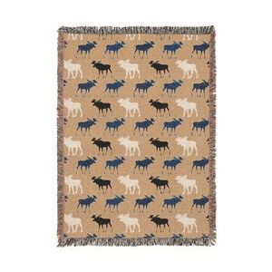May include: A rectangular woven throw blanket featuring a repeating pattern of moose silhouettes in navy blue, black, and cream colours against a tan background. The blanket has a textured weave and finished edges with a short, frayed fringe detail.