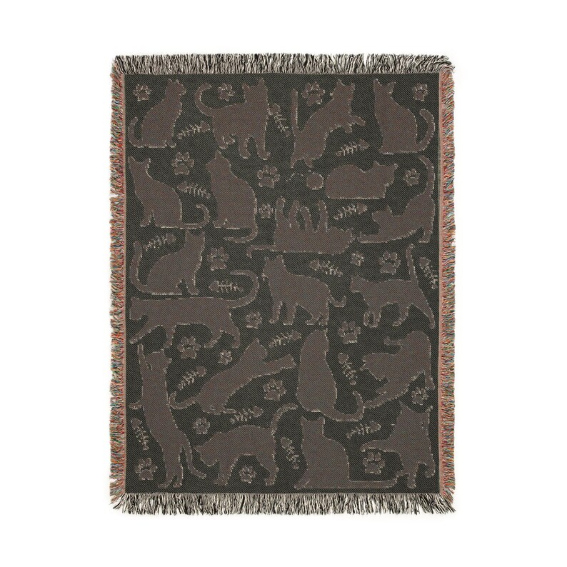 May include: A woven throw blanket featuring a repeating pattern of cat silhouettes in various poses, paw prints, and fish bones. The cats are a dark brown color against a dark gray background. The blanket has a fringed edge.