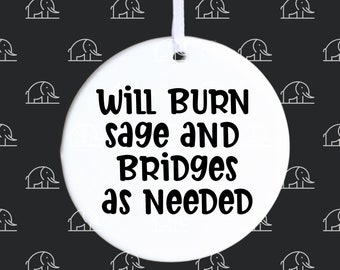 May include: White round ceramic ornament with black text that reads "Will Burn Sage and Bridges as Needed".