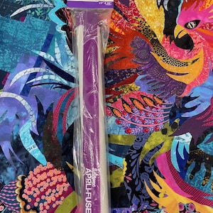 May include: A purple and white silicone Appli-Fuse mat, 17 x 24 inches, in a clear plastic package. The mat is labeled with the text "Silicone APPLI-FUSE MAT" and "GYPSY quilter". The background features a colorful, abstract fabric design.