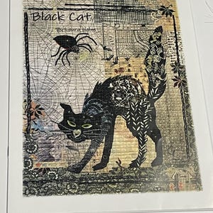 May include: A framed art print featuring a black cat with green eyes, arched back, and a decorative tail. The artwork includes a spider, bats, and a spiderweb. The text "Black Cat" and "By Laura Heine" are visible.