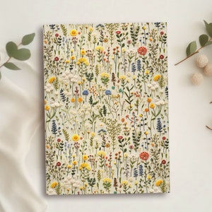 May include: A white notebook with a floral pattern embroidered on the cover. The flowers are in shades of yellow, red, blue, and green.