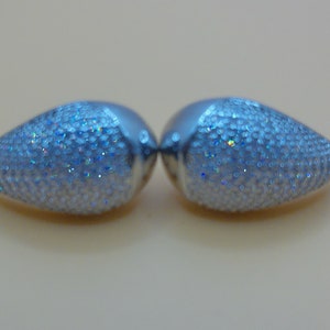 Op de afbeelding: Een paar zilveren, traanvormige oorbellen met iriserende glitter.