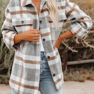 Puede incluir: Una sobrecamisa de manga larga con botones y estampado de cuadros en tonos gris, blanco y beige. La prenda incluye un cuello clásico, dos bolsillos en el pecho con solapas abotonadas y cierre frontal de botones, combinada con pantalones vaqueros azul claro.