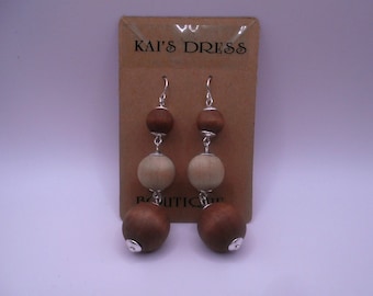 May include: A pair of wooden bead earrings with brown and beige beads. The earrings are hanging from a card that says "Kai's Dress Boutique".