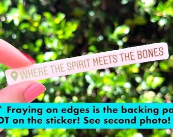 Peut inclure: Un autocollant blanc avec le texte "WHERE THE SPIRIT MEETS THE BONES" en lettres brunes. L'autocollant est tenu par une main. Le texte "*NOTE* Fraying on edges is the backing paper NOT on the sticker! See second photo!" est visible sous l'autocollant.