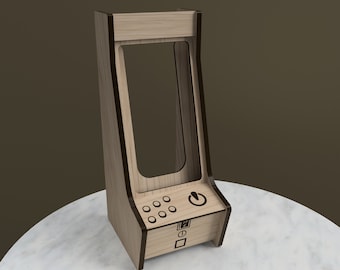 May include: A wooden arcade-style phone stand with a cutout for a phone and a control panel with buttons and a power button. The stand is made of light brown wood with dark brown trim.