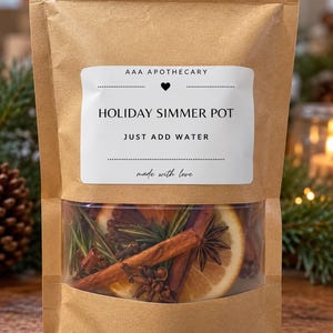 Può includere: Un sacchetto di carta marrone con una finestra trasparente contenente fette di arancia essiccata, bastoncini di cannella, anice stellato, chiodi di garofano e rosmarino. L'etichetta bianca riporta AAA APOTHECARY, HOLIDAY SIMMER POT, JUST ADD WATER, made with love.