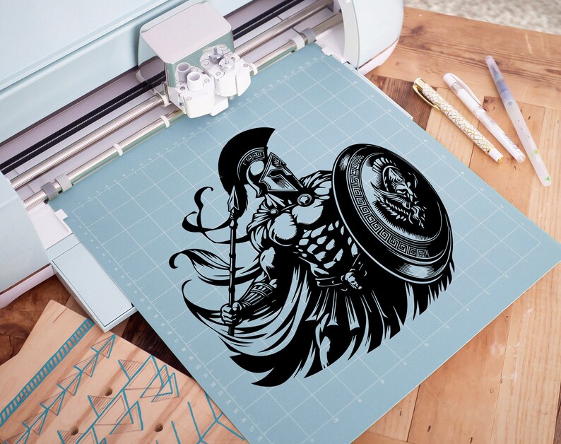 K&ouml;nnte beinhalten: Eine Schwarzwei&szlig;illustration eines griechischen Kriegers, der einen Speer und einen Schild h&auml;lt. Der Krieger tr&auml;gt einen Helm und eine R&uuml;stung. Die Illustration befindet sich auf einer blauen Schneidematte.