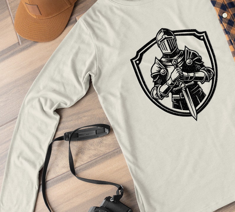 May include: A long-sleeved, light grey t-shirt with a black and white graphic of a knight in armour holding a sword, standing inside a shield.