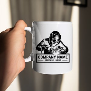 Op de afbeelding: Witte keramische mok met een zwart-witte illustratie van een lasser met een lasmasker en een lasbrander. De tekst "COMPANY NAME" staat onder de illustratie.