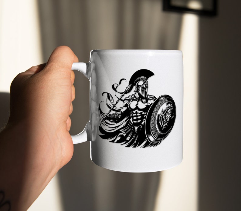 K&ouml;nnte beinhalten: Wei&szlig;e Keramiktasse mit einer Schwarzwei&szlig;illustration eines spartanischen Kriegers, der einen Speer und einen Schild h&auml;lt. Der Krieger tr&auml;gt einen Helm und eine R&uuml;stung.
