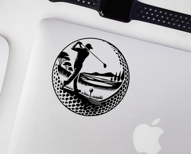 May include: Black and white golf-themed sticker showing a golfer in action within a golf ball design. The scene includes a golf course with trees, hills, and a tee. The sticker is placed on a white surface.