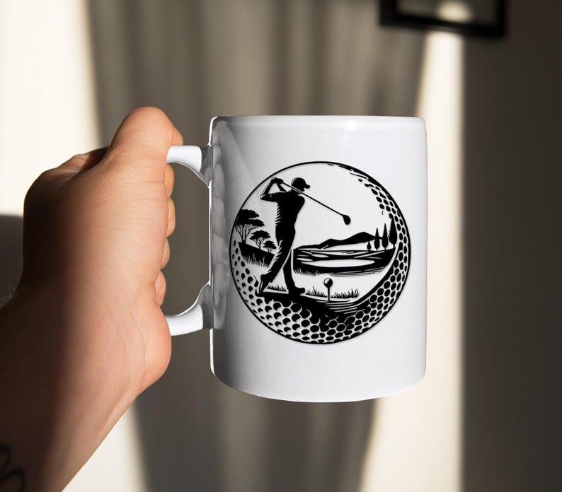 May include: White ceramic mug with a black and white golf design. The design shows a golfer swinging a club within a golf ball-shaped frame, with a golf course landscape. The mug has a curved handle.