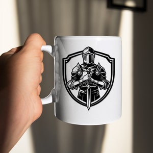 May include: White ceramic mug featuring a black and white illustration of a knight in armour holding a sword. The knight is standing in front of a shield.
