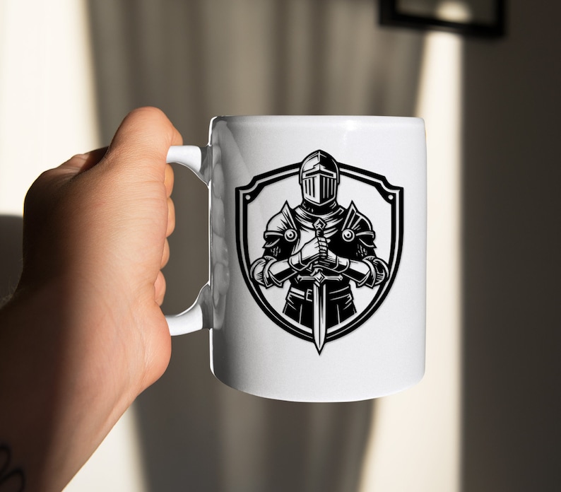 May include: White ceramic mug featuring a black and white illustration of a knight in armour holding a sword. The knight is standing in front of a shield.