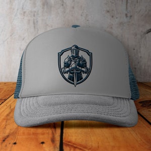 May include: Grey trucker hat with a blue embroidered design of a knight holding a sword in front of a shield.