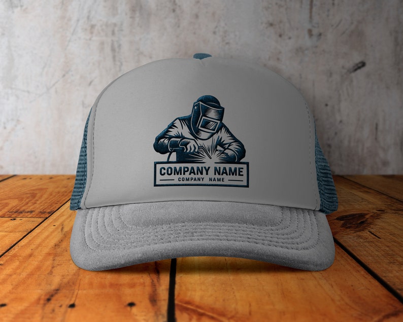 Op de afbeelding: Grijze truckercap met een blauw mesh achterpaneel. De voorkant van de cap heeft een zwart-witte illustratie van een lasser met een lasmasker en de tekst "COMPANY NAME COMPANY NAME".