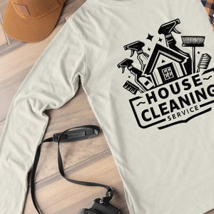 May include: A white long-sleeved t-shirt with a black graphic design of a house with cleaning supplies and the text "HOUSE CLEANING SERVICE".