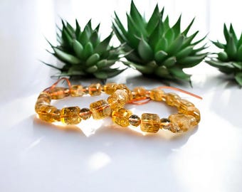 May include: Two bracelets made of orange and brown gemstone beads. The beads are square shaped and strung on a thin orange cord.