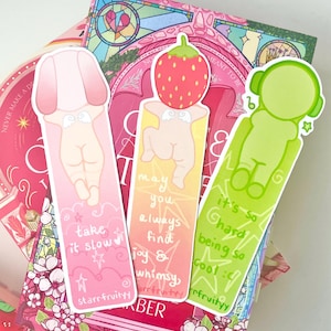 May include: Three colorful bookmarks with whimsical illustrations and text. One pink bookmark says "take it slow" and another says "may you always find joy & whimsy". The third is green and says "it's so hard being so cool".