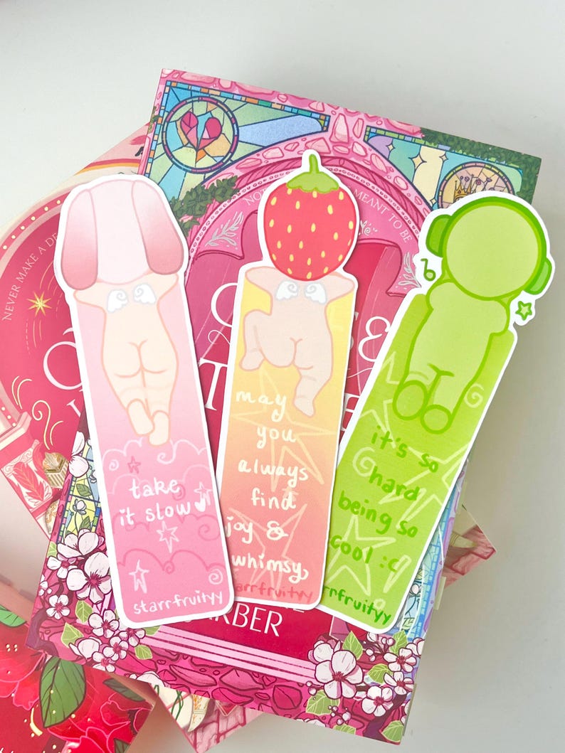 May include: Three colorful bookmarks with whimsical illustrations and text. One pink bookmark says "take it slow" and another says "may you always find joy & whimsy". The third is green and says "it's so hard being so cool".