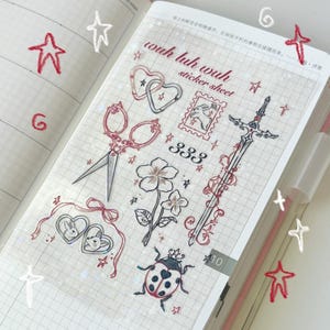 May include: A clear sticker sheet featuring a variety of illustrations, including a pair of scissors, a flower, a sword, a ladybug, and a locket with two rabbits. The sheet has a grid pattern and the text "wuh luh wuh sticker sheet" is printed on it.