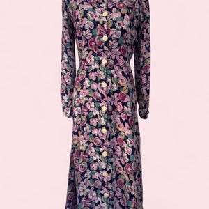 May include: A long-sleeved midi dress featuring a dark navy blue base with an all-over floral pattern in shades of pink, light purple, and green. The dress has a collared neckline, a full-length front button placket with round white buttons.