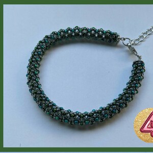 May include: A green and black beaded bracelet with a silver clasp. The bracelet is made with small, iridescent beads.