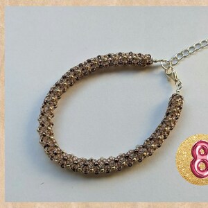 May include: A brown and gold beaded bracelet with a silver clasp. The bracelet is made with small, round beads that are arranged in a pattern. The bracelet is about 8 inches long.