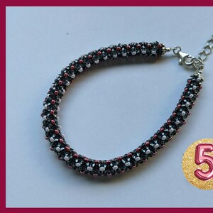 May include: A black, white, and red beaded bracelet with a silver clasp. The bracelet is made with small, round beads and has a simple design.
